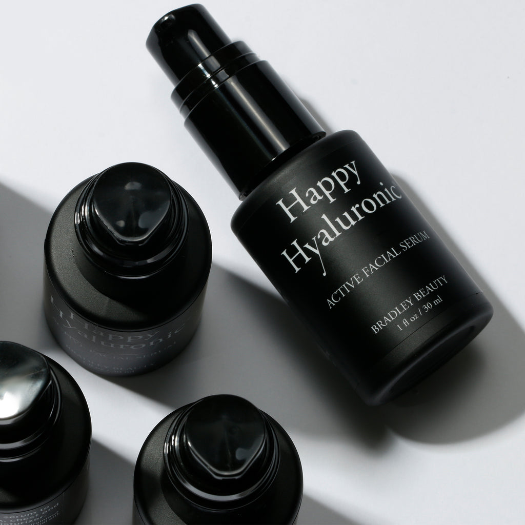 An overhead point of view showing the tops of three Happy Hyaluronic bottles and one bottle lying face up.