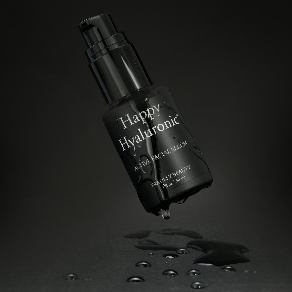 Floating bottle of Happy Hyaluronic dripping wet against a black background.