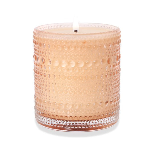 The Perfect Blend of Fig with a lit wick in a peach tinted bubbled glass vessel.